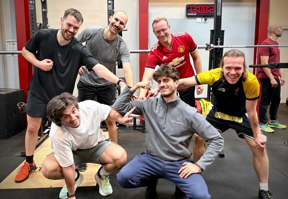 Un groupe d'hommes souriants partage un moment de convivialité dans une salle de musculation équipée de racks.