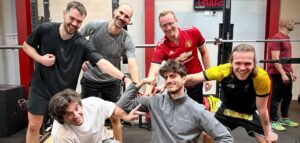 Un groupe d'hommes souriants partage un moment de convivialité dans une salle de musculation équipée de racks.