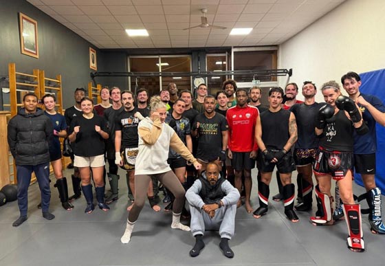 Un grand groupe de pratiquants de sports de combat pose ensemble sur un tatami, équipés de gants et de protège-tibias.