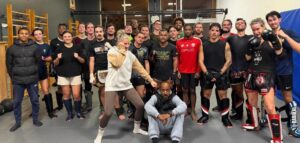Un grand groupe de pratiquants de sports de combat pose ensemble sur un tatami, équipés de gants et de protège-tibias.