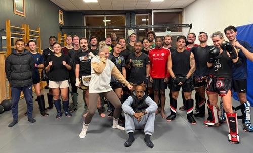 Un grand groupe de pratiquants de sports de combat pose ensemble sur un tatami, équipés de gants et de protège-tibias.